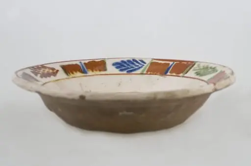 Vas ceramic de formă tronconică baza plată, pereții larg evazați și buza profilată. După modelarea la roată, uscarea și arderea recipientului, a fost aplicat un strat de angobă în interiorul vasului, peste care a fost pictat decorul floral și vegetal stilizat, format din două registre. În primul registru, situat pe fundul vasului și încadrat de o linie circulară, au fost realizate trei flori, cu petale albastre și mijlocul maro-roșcat, în jurul cărora se regăsesc petale verzi. Cel de-al doilea registru, cel care decorează buza vasului și este încadrat la rândul lui între două linii circulare, a fost decorat cu frunze și pete, despărțite de linii verticale. Cromatică: fond: alb; motive: maro-roșcat; albastru; verde., by Unknown