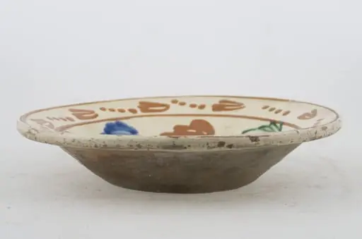 Vas ceramic de formă tronconică cu baza plată, pereții larg evazați și buza profilată. După modelarea la roată, uscarea și arderea recipientului, a fost aplicat un strat de angobă în interiorul vasului, peste care a fost pictat decorul floral și vegetal stilizat, format din două registre. Primul registru, situat pe fundul și pereții vasului, și încadrat de o linie circulară, a fost decorat cu motive florale stilizate: pe fundul vasului se află o floare, cu petalele de diferite culori. Pereții recipientului ceramic au fost decorați la rândul lor cu opt flori, dispuse concentric. Al doilea registru, cel care decorează buza recipientului ceramic, și este mărginit la rândul lui de o linie circulară, prezintă un brâu compus din nouă flori cu tulpinile formate din patru puncte. Cromatică: alb la interior; cărămiziu la exterior; motive: albastru; verde; maro-roșcat., by Unknown