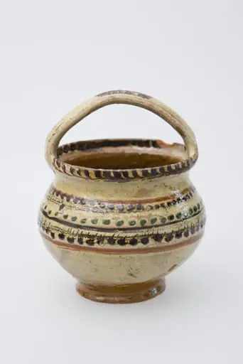 Vas ceramic de mici dimensiuni, pe bază inelară, pântecos, cu fundul și gura late. Deasupra gurii vasului a fost pusă o toartă de prindere. Buza vasului a fost pictată printr-un brâu de crenguțe. Pe pântecul vasului brâuri de puncte și două benzi subțiri jirăvite. Smălțuit în interior și exterior. Cromatică: fond: crem; motive: verde; maro; bej., by Unknown