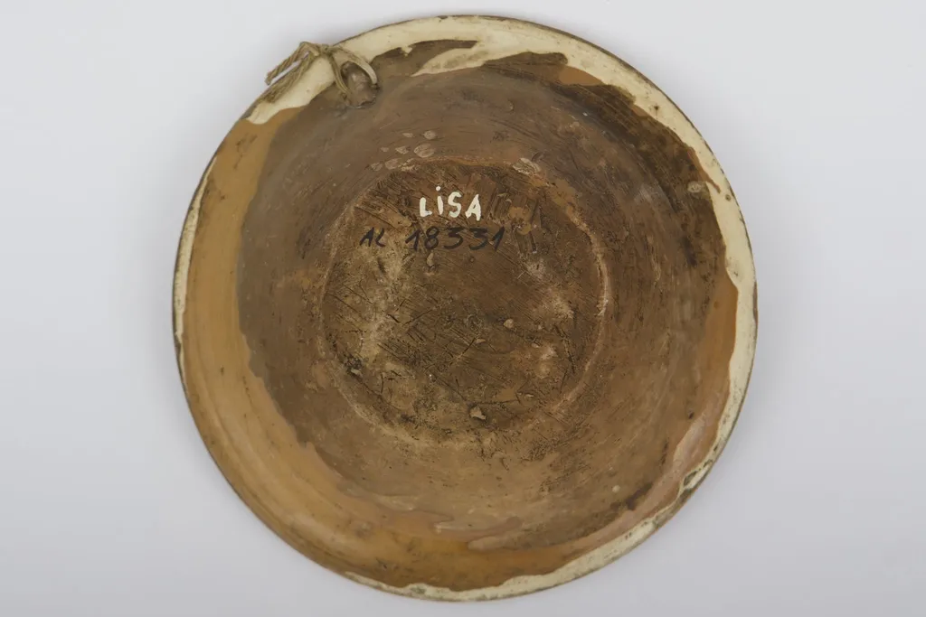 Vas ceramic smălțuit la interior, de formă tronconică, cu fundul plat, pereții ridicați și marginea evazată. Farfuria prezintă decor geometrizant și fitomorf stilizat. Pe fundul vasului, peste stratul crem de angobă, au fost realizate patru flori maro, cu mijlocul verde și albastru, fiind mărginite de patru grupuri a câte nouă puncte verzi și albastre (două câte două, în diagonală). Cel de-al doilea registru pictural a fost realizat marginal, pe buza piesei; fiind încadrat între două linii circulare drepte un șir de „V-uri” succesive. Farfuria era folosită în gospodărie pentru decorarea interioarelor sau servirea hranei. Prezintă uzură funcțională: Cromatică: fond: cărămiziu; crem; motive: maro; verde; albastru., by Unknown, unspecified, 1850