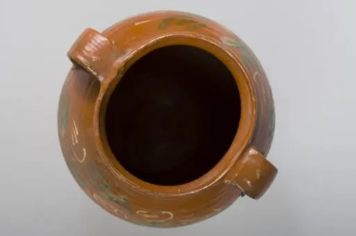 Vas de formă bitronconică, cu gât scurt cu buză rotunjită și evazată. Oala este smălțuită interior și pe 2/3 din exterior. Prezintă două toarte late ce unesc buza vasului de zona diametrului maxim. Decorații în registru floral-vegetal, dispuse concentric, în partea superioară a vasului, compuse din linii ondulate și palmate. Cromatică: fond: cărămiziu; motive: alb, verde., by Unknown