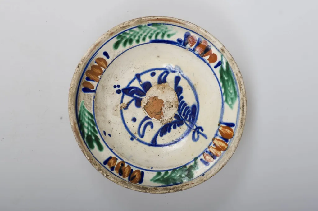 Vas de formă tronconică adâncit, smălțuit în interior cu buză profilată spre exterior. Este decorat în interior cu motive vegetale și florale (motivul brăduțului) dispuse într-un registru circular pictat pe în zona diametrului maxim al vasului. Cromatică: fond cărămiziu (exterior) cu scurgeri de smalț alb spre baza vasului; fond crem (interior); albastru; maro; verde; galben., by Unknown, 1850