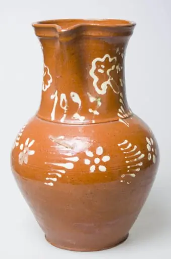 Vasul are forma tronconică, cu fund lat, gât gros, toartă și cioc opus acesteia. Decorul este unul floral, stilizat pe partea superioară imediat sub cioc. Obiectul este smălțuit pe ambele părti, fiind prevăzut cu o toartă pentru prindere. Cromatică: fondul este maro, iar motivele sunt pictate cu alb., by Unknown
