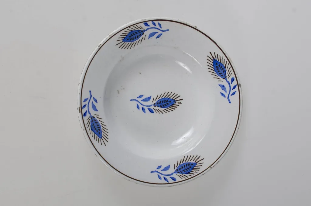 Vasul prezintă formă tronconică adâncită cu o bordură decorată cu motive florale și vegetale dispuse câte două în opoziție pe suprafața buzei (patru flori cu frunze). În centru este decorat cu o floare. Prezintă o marcă indescifrabilă pe exteriorul vasului. Cromatică: fond: alb; motive: albastru; maro., by Unknown, 1850