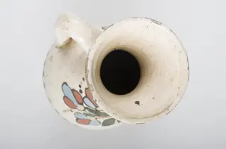 Vas bitronconic, cu gât arcuit spre interior și gura evazată spre exterior. O toartă unește mijlocul gâtului de mijlocul corpului. Vasul este decorat cu motive vegetale și florale prin pictare. Registrul decorativ principal este reprezentat de o floare cu petale și frunze alungite. Gâtul vasului este decorat cu motive geometrice (triunghiuri, arcuri de cerc, puncte, linie vălurită). Partea inferioară a vasului este decorat în aceeași manieră ca și gâtul. Vasul prezintă smălțuire. Cromatică: fond: alb; motive: roșu; albastru; verde; galben., 1850