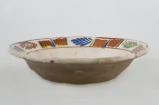 Vas ceramic de formă tronconică baza plată, pereții larg evazați și buza profilată. După modelarea la roată, uscarea și arderea recipientului, a fost aplicat un strat de angobă în interiorul vasului, peste care a fost pictat decorul floral și vegetal stilizat, format din două registre. În primul registru, situat pe fundul vasului și încadrat de o linie circulară, au fost realizate trei flori, cu petale albastre și mijlocul maro-roșcat, în jurul cărora se regăsesc petale verzi. Cel de-al doilea registru, cel care decorează buza vasului și este încadrat la rândul lui între două linii circulare, a fost decorat cu frunze și pete, despărțite de linii verticale. Cromatică: fond: alb; motive: maro-roșcat; albastru; verde.
