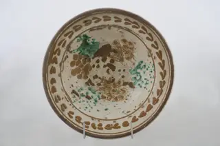Vas ceramic de formă tronconică cu baza plată, pereții larg evazați și buza dreaptă și înălțată. După modelarea la roată, uscarea și arderea recipientului, a fost aplicat un strat de angobă în interiorul vasului, peste care a fost pictat decorul floral și vegetal stilizat, format din două registre. Primul registru, situat pe fundul și pereții vasului, și încadrat de o linie circulară, a fost decorat cu câte trei pete mari de culoare verde și galben-muștar, realizate prin stropire cu pensula. Al doilea registru, cel care decorează buza recipientului ceramic și este mărginit, la rândul lui de o linie circulară, prezintă elemente ornamentale de tipul „bobului de grâu”. Cromatică: fond: alb; motive: roșu; albastru; verde.