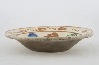 Vas ceramic de formă tronconică cu baza plată, pereții larg evazați și buza profilată. După modelarea la roată, uscarea și arderea recipientului, a fost aplicat un strat de angobă în interiorul vasului, peste care a fost pictat decorul floral și vegetal stilizat, format din două registre. Primul registru, situat pe fundul și pereții vasului, și încadrat de o linie circulară, a fost decorat cu motive florale stilizate: pe fundul vasului se află o floare, cu petalele de diferite culori. Pereții recipientului ceramic au fost decorați la rândul lor cu opt flori, dispuse concentric. Al doilea registru, cel care decorează buza recipientului ceramic, și este mărginit la rândul lui de o linie circulară, prezintă un brâu compus din nouă flori cu tulpinile formate din patru puncte. Cromatică: alb la interior; cărămiziu la exterior; motive: albastru; verde; maro-roșcat.