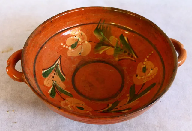 Vas de formă tronconică, cu două toarte laterale („cu urechi”) și una mică la spate. Decor geometric și floral stilizat: între două cercuri concentrice (unul pe fundul vasului, iar cel de-al doilea în partea superioară), trei flori cu frunze stilizate. Cromatică: roșu, negru, verde, alb, galben. Timp de lucru: circa două săptămâni.